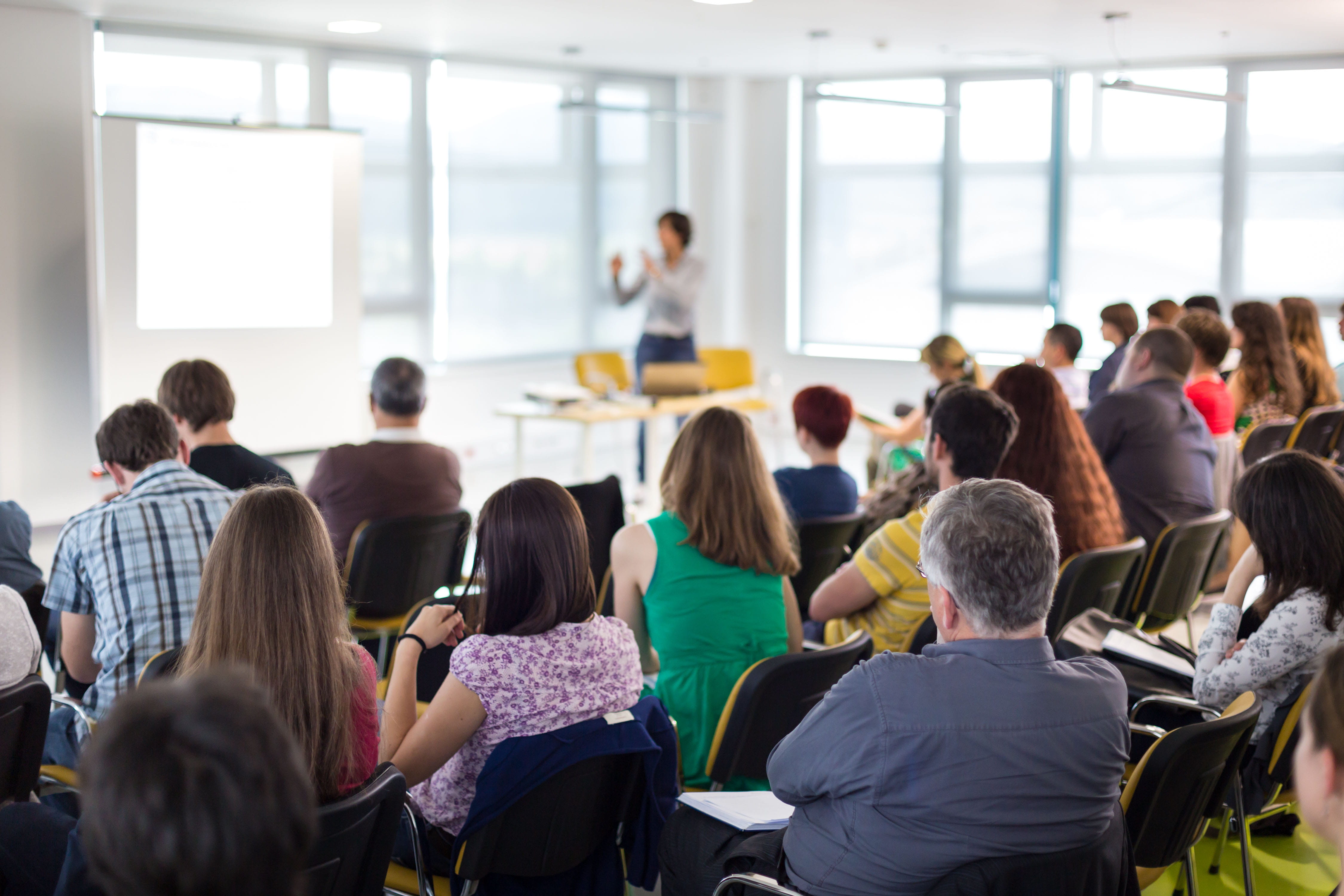 Instructor stands in a classroom, addressing a room of adults.